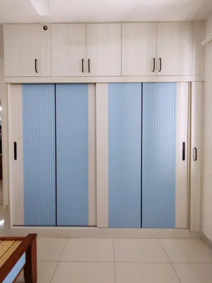 This modern wardrobe features sliding doors with frosted blue panels, a great space-saving solution for smaller bedrooms. The overhead cabinets provide additional storage, making full use of the vertical space.