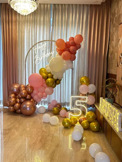 A stylish fifth birthday party with an organic balloon garland in rose gold, pink, and peach. The setup includes a neon sign and marquee letters and numbers.