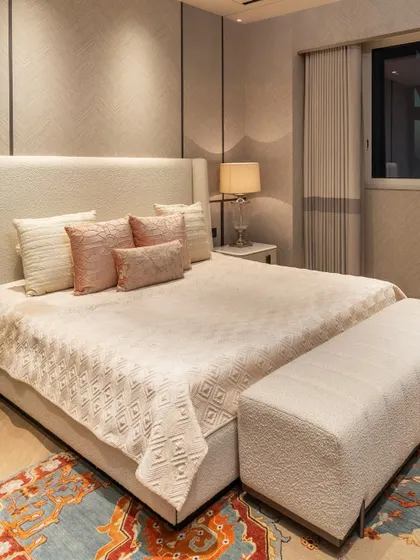 This guest bedroom features a serene palette of creams and soft pinks. The custom upholstered bed and matching bench are set against a textured wallpaper, creating a harmonious and restful space for visitors.