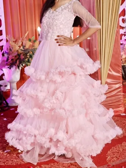 This baby pink ball gown is pure romance. It features a delicately beaded bodice with sheer sleeves and a full, tiered skirt of soft ruffles.