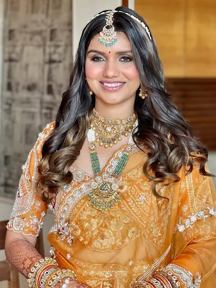 A full view of the Phera look. The orange lehenga is paired with soft, glowing makeup and beautiful, voluminous curls.