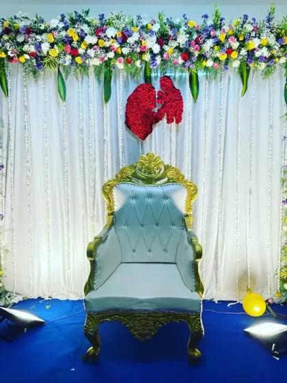An elegant and coustamised baby shower decoration featuring a beautiful floral frame, a white throne chair, and a backdrop of white curtains with crystal strings.
