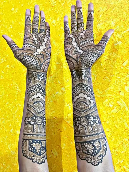 This reverse-fill or negative space mehndi design creates a dramatic and beautiful effect. The floral and paisley patterns are left empty while the background is filled in, making the main motifs stand out.