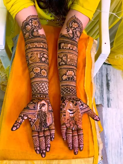 This full-arm design tells a story in bands, featuring portraits of a bride and groom, elephants symbolizing good luck, and beautiful peacock and lotus motifs.