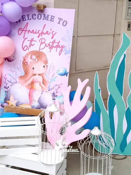 A charming welcome display with a personalized sign for Anaisha's 6th birthday, surrounded by pastel balloons, coral cutouts, and white birdcages for a whimsical touch.
