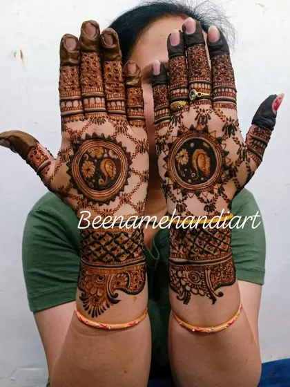 A happy client showing off her full bridal mehandi. The design features peacock mandalas on the palms and a dense jaal pattern on the arms.