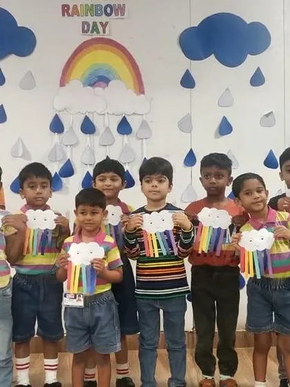 Students hold up their rainbow crafts in front of a beautifully decorated wall, celebrating Rainbow Day in their classroom.