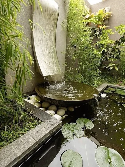 We create tranquil water features that bring a sense of calm to any garden. This design features a modern sculpted waterfall flowing into a small pond with lily pads, surrounded by bamboo and other moisture-loving plants for a complete sensory experience.