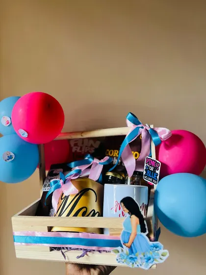 A lovely gift crate for an expecting mother. This hamper includes personalized "Mom" mugs and a variety of snacks, decorated with pink and blue balloons for a festive baby shower feel.
