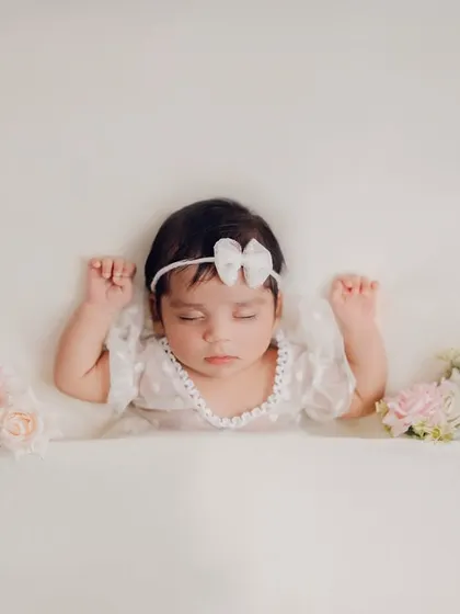 A sweet angel sleeping on a cloud of white. This minimalist setup with delicate pink and white roses on either side creates a dreamy and pure portrait of a newborn baby.