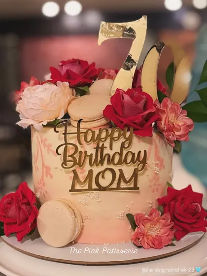 A heartfelt 70th birthday cake for a mom. This pretty pink cake is adorned with fresh red and pink roses, macarons, and a gold acrylic "Happy Birthday Mom" topper.