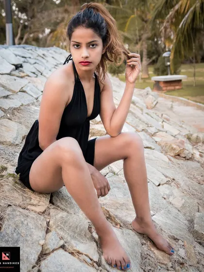 A seated portrait from the 'Boho' series. The model sits barefoot on the rocks, her direct gaze and the natural background capturing a raw and bohemian style.