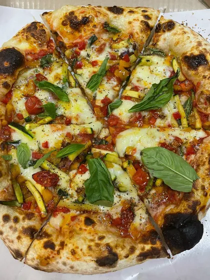 A vibrant veggie pizza with zucchini, cherry tomatoes, and fresh basil leaves. The colors are as amazing as the taste.