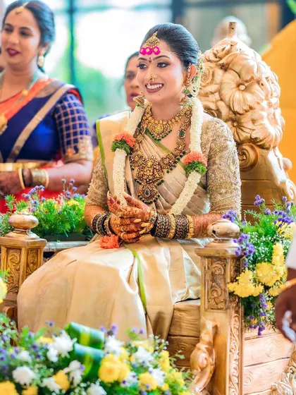 A regal shot of the bride on her throne. Her gold Kanchivaram saree and custom blouse create a look of timeless elegance.