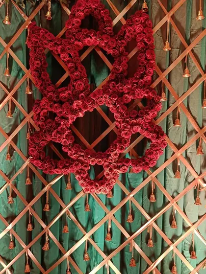I can also create custom designs with flowers. This piece features a symbol made entirely of red roses, set against a green backdrop with hanging bells, for a very traditional and meaningful decoration.