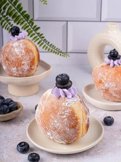 Fluffy bomboloni donuts with a blueberry cream topping, styled in a clean, bright setting.