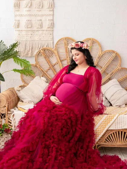 A portrait of pure elegance. Seated on our boho set, this mother-to-be is stunning in a deep magenta ruffled gown, embodying a sense of luxury and high fashion.