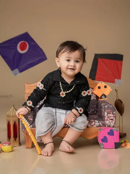 A baby boy in a black kurta and white dhoti, surrounded by kites and lanterns. This setup combines traditional elements for a perfect Sankranti portrait.