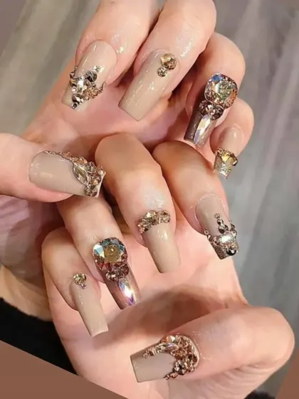 The definition of luxury. These long, square-shaped nails feature a nude base and are heavily adorned with an array of gold and iridescent rhinestones in various shapes and sizes for a truly decadent look.