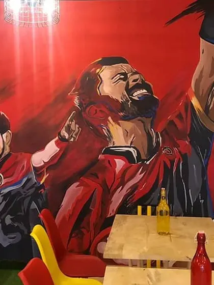 The finished RCB mural in its full glory at the Ee Sala Cup Namde Cafe. The bright red background and dynamic poses make the whole space feel energetic.