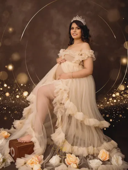 An angelic portrait of an expectant mother seated in a cream-colored ruffled gown. The scene is accented with soft lighting, a golden halo backdrop, and scattered roses for a heavenly feel.