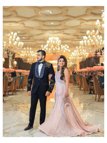 A wide shot of the couple in a grand, empty ballroom, filled with crystal chandeliers. This pre-event portrait captures the scale and opulence of their reception venue.