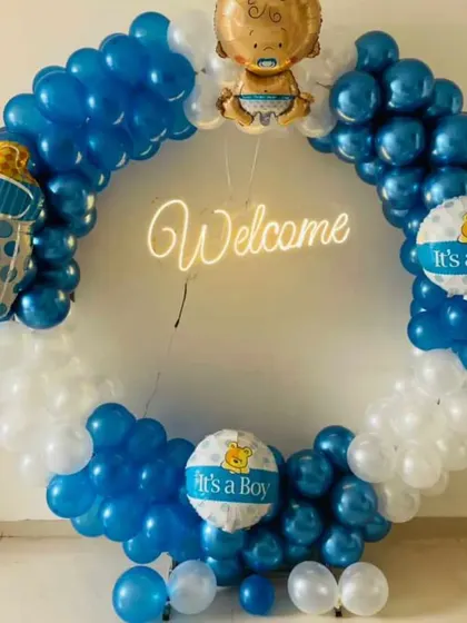 For a modern and stylish welcome for your baby boy, I offer these circular balloon arches with a "Welcome" neon sign. This setup uses blue and white balloons, "It's a Boy" themed foils, and a cute baby foil balloon on top. I can set this up in your home in Delhi NCR.