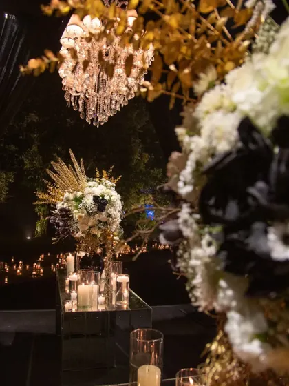 A view of the black, white, and gold arrangements under a sparkling crystal chandelier. The combination of different light sources, from candles to electric light, creates a dynamic and layered ambiance.