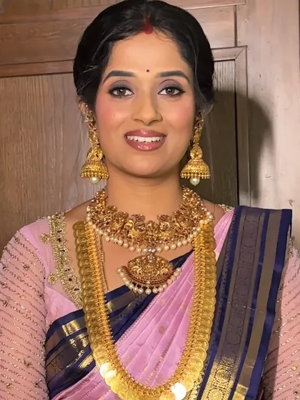 A lovely traditional look in a pink and blue silk saree. The makeup is soft and glowing, paired with a classic braided hairstyle featuring a criss-cross gold ribbon detail and fresh flowers.