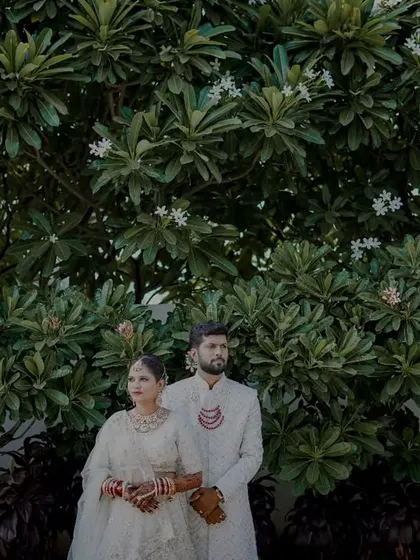 A powerful, symmetrical portrait of the couple standing before a large, dense green hedge, creating a striking visual contrast.