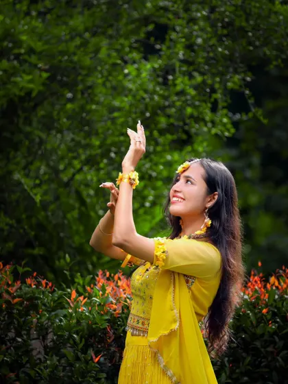 A beautiful outdoor portrait of a bride-to-be during her Haldi, looking up with a happy expression amidst lush greenery.