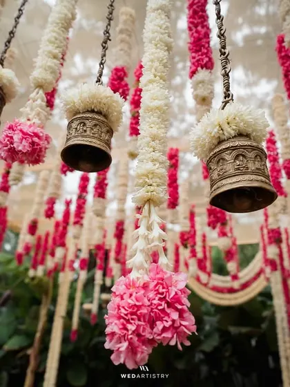 A beautiful close-up of hanging floral tassels and brass bells, a detail that adds texture and traditional elegance to the wedding decor.