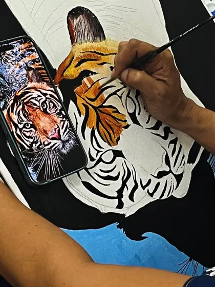A close up of a student painting a realistic tiger, using a photo reference to capture every detail of the fur and stripes.