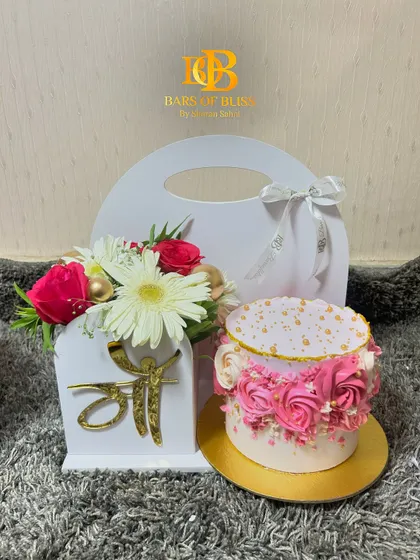A beautiful Mother's Day gift set featuring a floral cake with pink rosettes and a matching floral arrangement in a custom "Maa" holder.