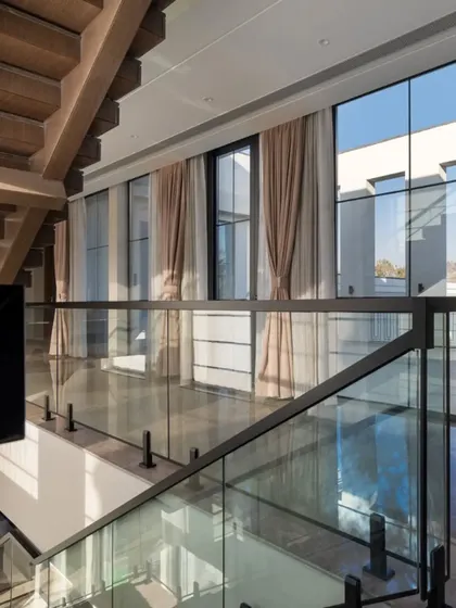 Looking down from the staircase landing, this view captures the double-height windows and the seamless flow of space. The glass railings ensure that views and light are unobstructed.