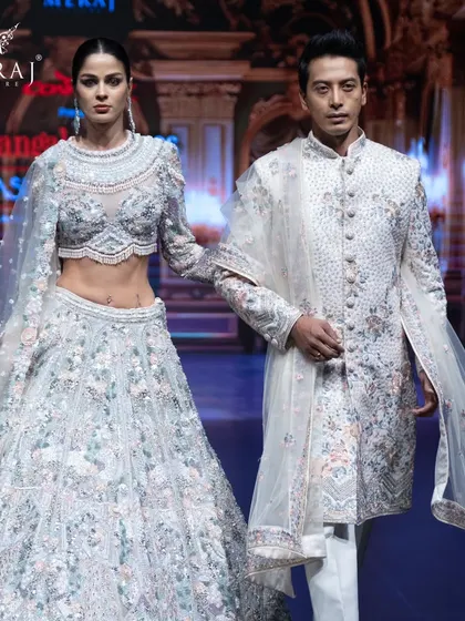 This image captures the grace of the off-white bridal lehenga and men's sherwani. The groom's outfit is a study in subtle, exquisite floral multicolor embellishments.