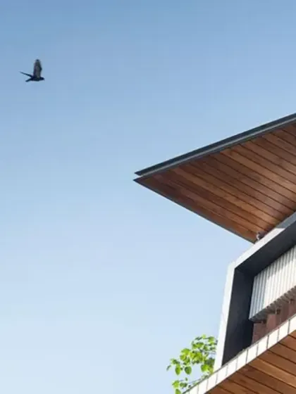 The elevation of J House is shaped by its interior functions, with carved-out blocks forming sheltered terraces. An abstract cantilevered roof in warm wood tones crowns the façade, giving it a bold and contemporary character.