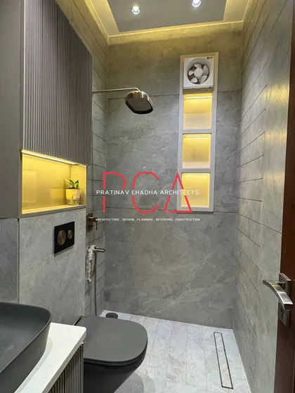 A still shot of the minimalist modern bathroom, featuring grey marble-finish tiles, a wall-mounted toilet, and a sleek black sink.