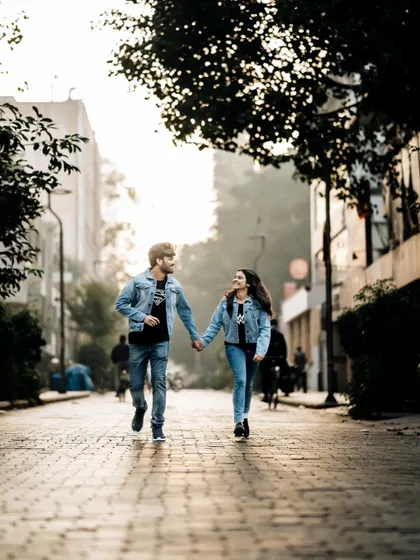 A dynamic shot of a couple in matching denim jackets running hand-in-hand down a city street at sunrise, capturing urban romance.