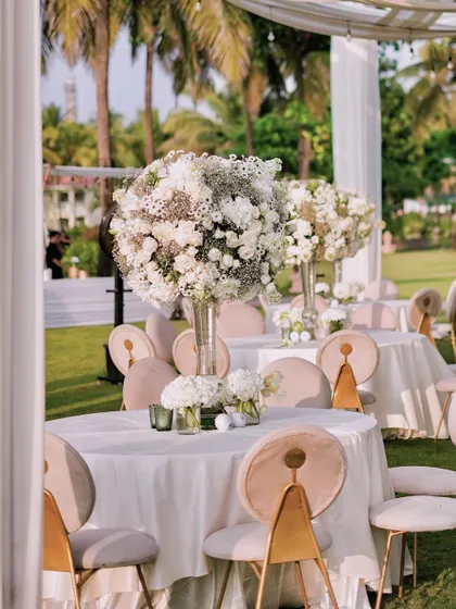 A soft-focus shot of the outdoor reception tables, highlighting the dreamy, romantic quality of the all-white floral decor. The palm trees in the background firmly place this beautiful celebration in a tropical paradise.