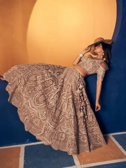 An artistic shot of a heavily embroidered bronze-gold lehenga. The unique pose highlights the incredible detail and craftsmanship of the skirt.