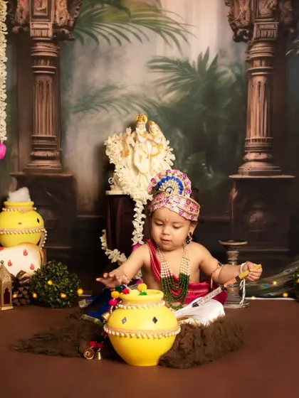 A playful shot of a baby Krishna sitting with his pot of butter, surrounded by festive props.