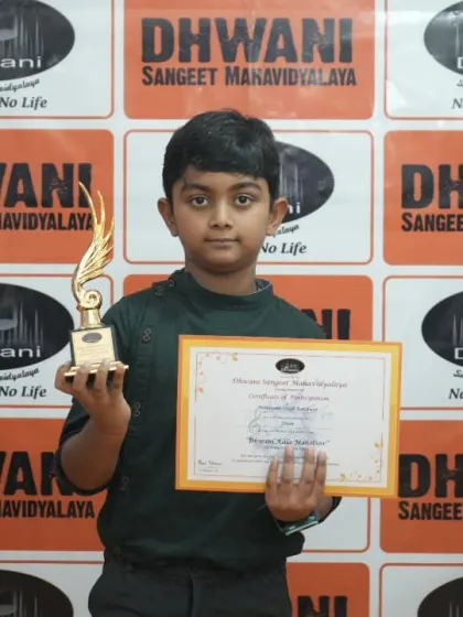 A young student proudly holds his certificate and trophy against the Dhwani backdrop.
