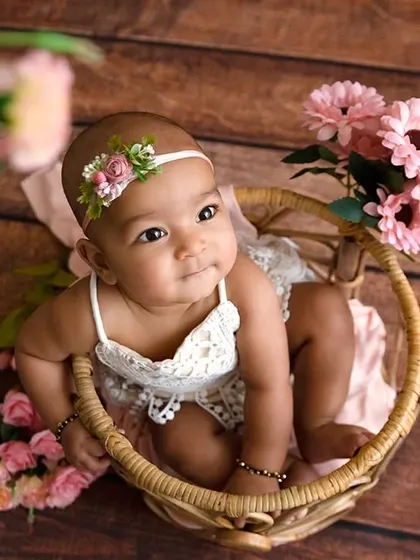A high-angle shot of a baby girl in a wicker basket, framed by pink flowers.