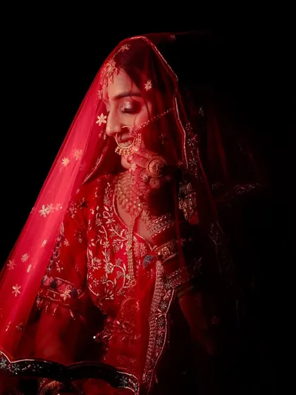 A dramatic, low-key bridal portrait, with the red of her veil providing a pop of color in the darkness.