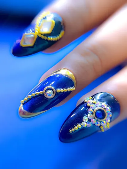 Another detailed shot of the royal blue nails, focusing on the different patterns on each nail, from simple crystal clusters to elaborate gold-framed designs.