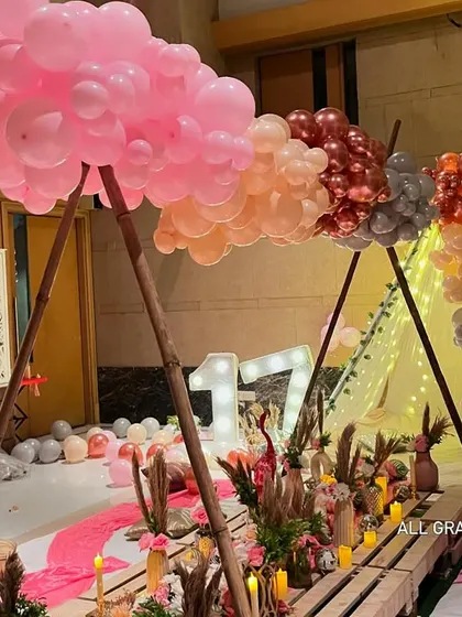 The A-frame structure over the picnic table is decorated with a cloud of pink, peach, and silver balloons, creating a stunning focal point.