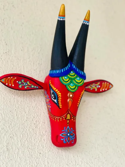 This bold red Nandi is adorned with blue and green peacock-feather-like scales, a classic color combination in Indian folk art.