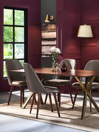 A full dining room scene designed to feel both elegant and welcoming. The deep plum walls create a sophisticated backdrop for the wooden dining set, allowing the furniture's form and finish to stand out.