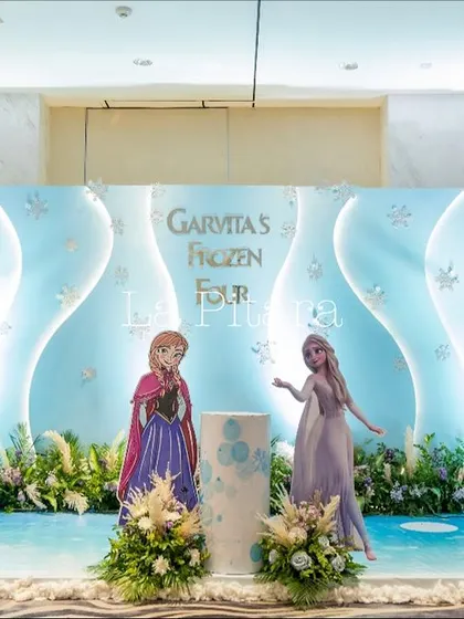 The main stage for a 'Frozen' party, designed to look like a scene from Arendelle. The backdrop features ice-like structures and beloved characters Anna and Elsa, creating an immersive experience for the birthday girl.